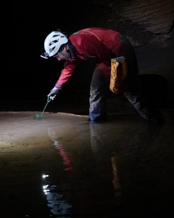 Man standing in cave, taking sample from water.