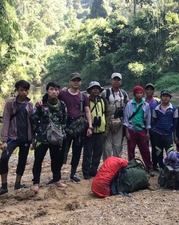 Group of 12 people standing in front of river, facing camera.