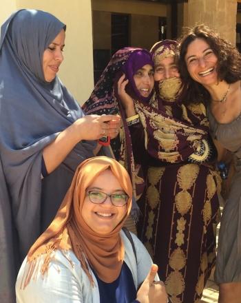 Group of about 8 women, most wearing head scarves, smile at camera.
