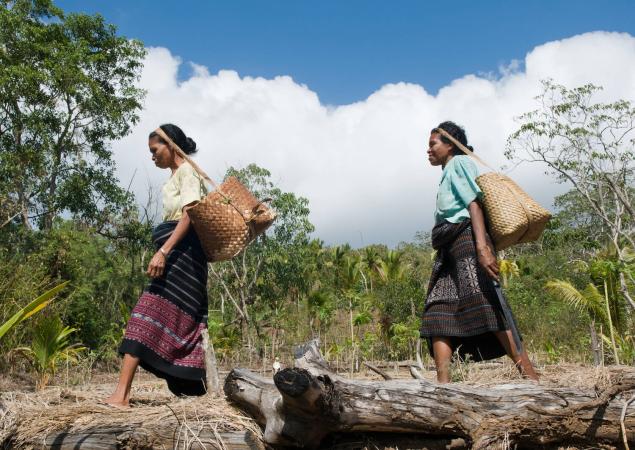 Deux femmes marchant, portant des sangles de sacs tissés sur la tête.