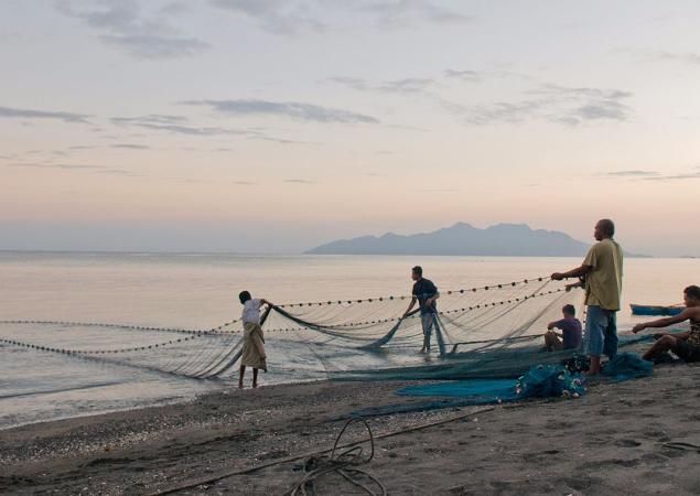 Un pequeño grupo de hombres se paran en una playa, sacando una gran red del agua, Isla de Flores, Indonesia.