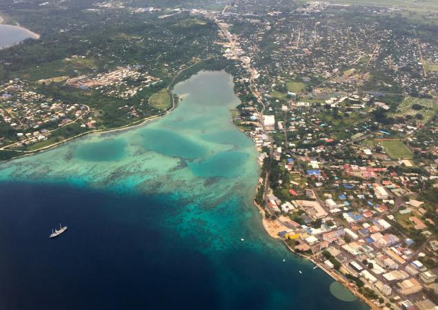 View of water, with a cruise ship, and island, with many buildings, from plane.