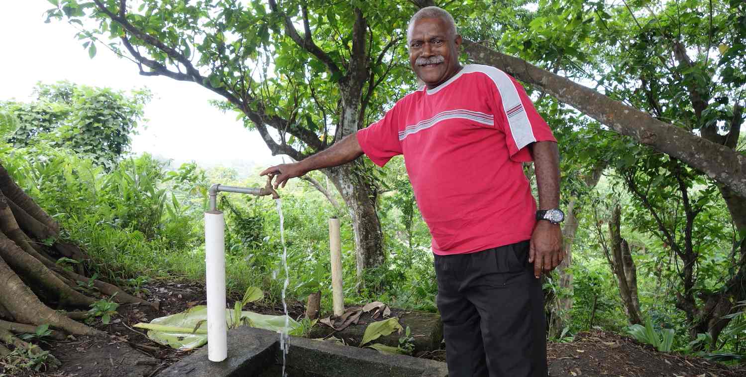 Un homme dans une zone boisée de la province de Tafea, au Vanuatu, utilise un robinet d'eau.