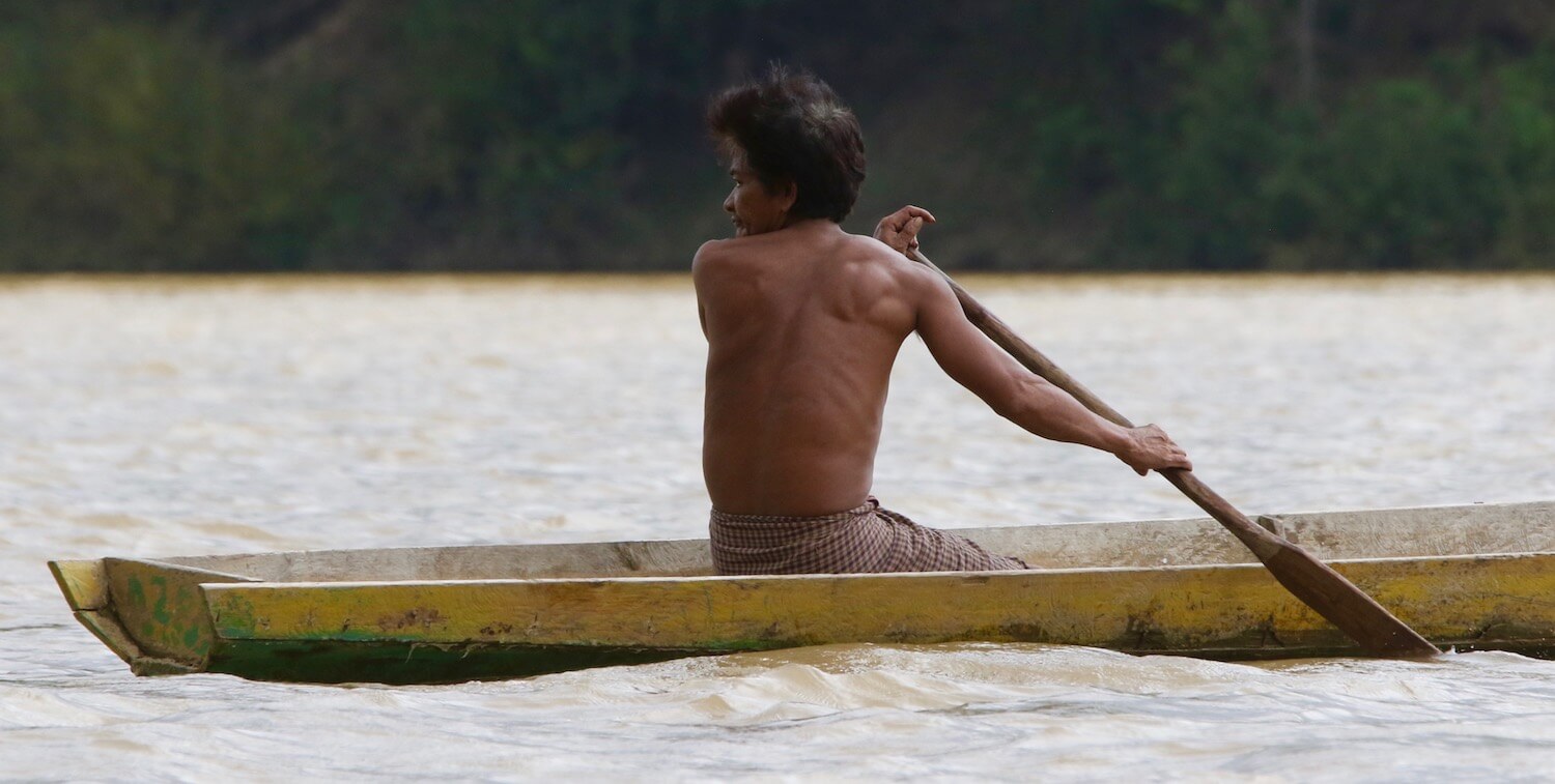 Man paddling wooden canoe, looks behind him.