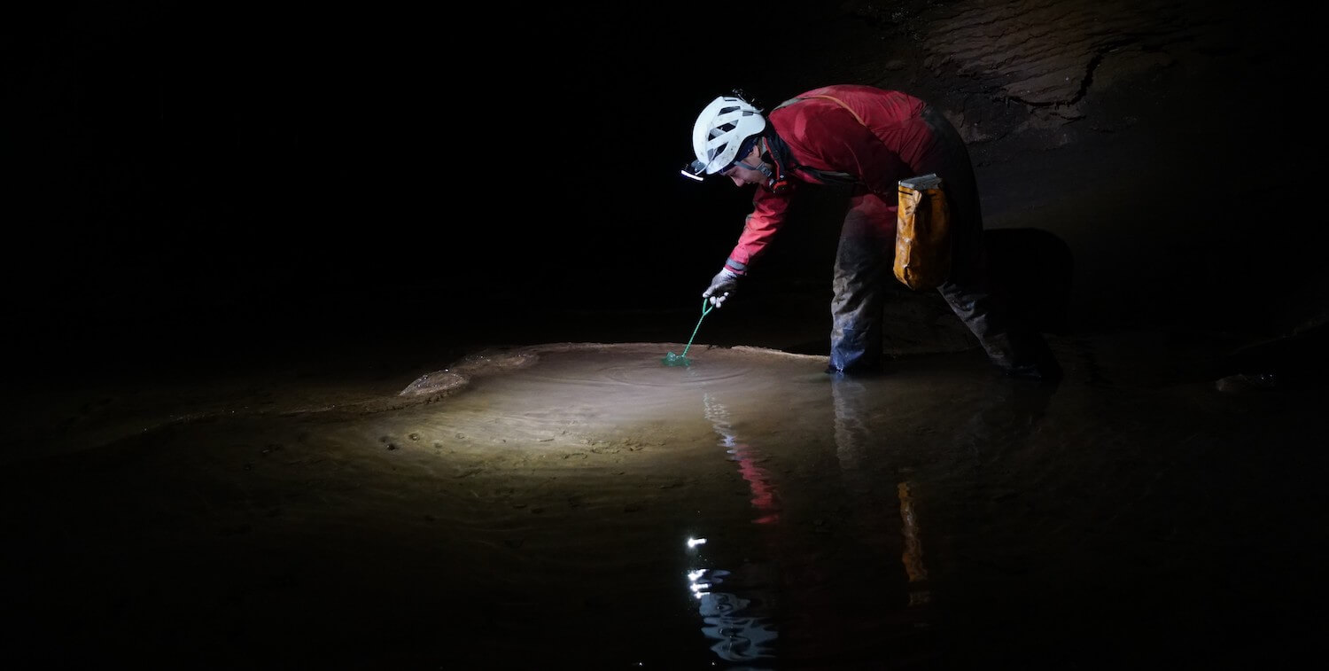 Man standing in cave, taking sample from water.