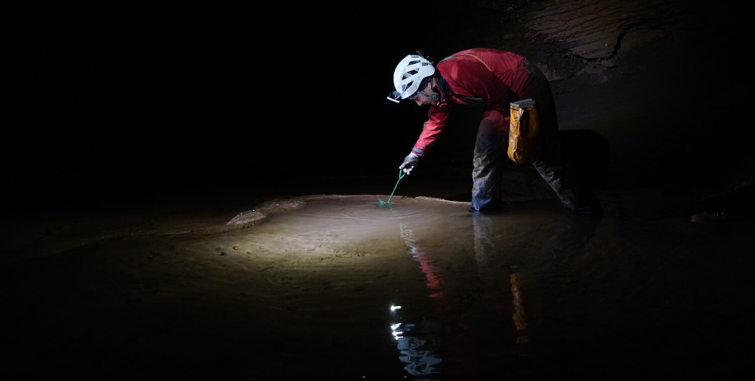 Hombre parado en una cueva, tomando muestras del agua.