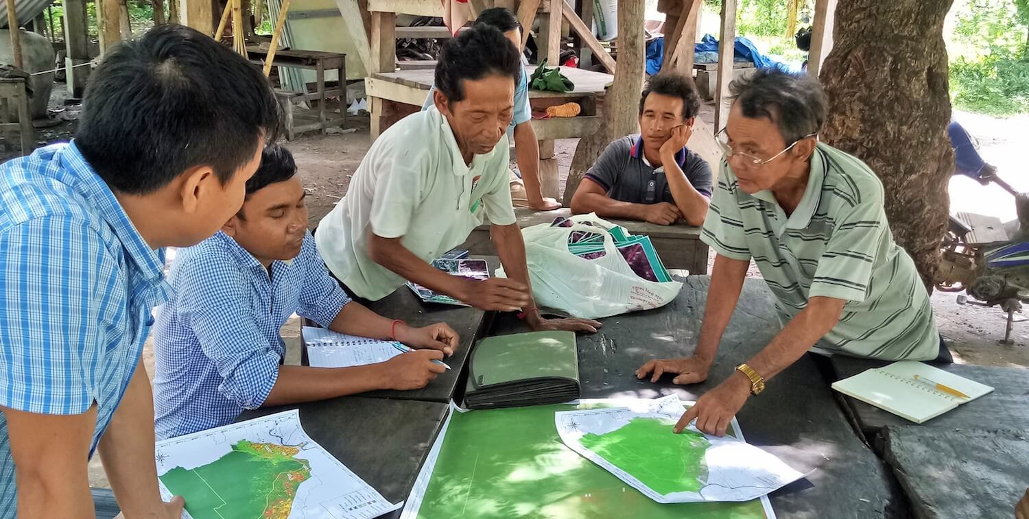 Handful of men outside looking at green maps on a table.