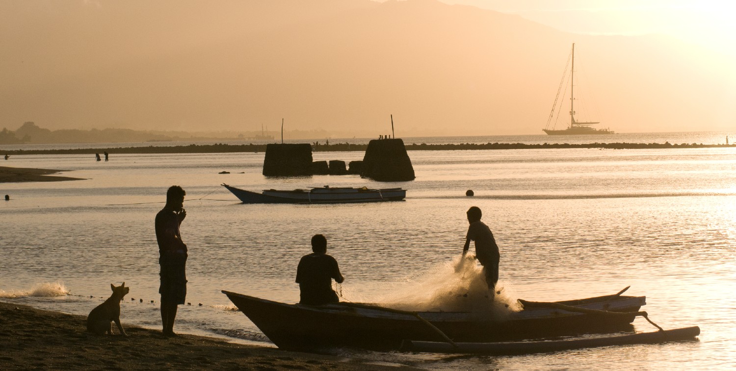 Two fishermen pulling nets into boat